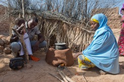 A woman cooks food with her husband and child at their home in a village near Zinder, Niger. The Irish Red Cross have been supporting labour-saving and environmentally-friendly initiatives in the area such as the use of fuel efficient stoves for cooking.